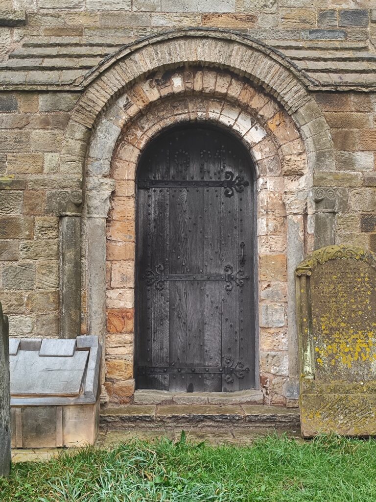 Norman archway in side of church with wooden door infill.